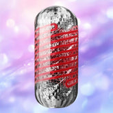 The Tenga Spinner DX 03 Steps by Tenga is a metallic, cylindrical male masturbator featuring a textured, reflective surface with red wavy lines, shown against a soft-focus purple and pink bokeh background.